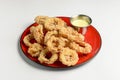 Golden onion rings and sauce in a saucepan served on a red plate. Isolated on white background. Royalty Free Stock Photo