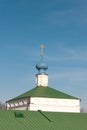 A golden orthodox cross on top of a blue dome on top of the stone white church with a green roof against a blue clear sky Royalty Free Stock Photo