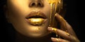 Golden paint smudges drips from the face lips and hand, golden liquid drops on beautiful model girl`s mouth, creative makeup Royalty Free Stock Photo
