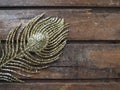 Golden peacock feather. Decorative gilded branch in the shape of a peacock's tail and eyelet. Wooden background