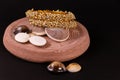 Golden pearl bangles with spreaded seashells on sand stone on black background