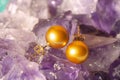 Golden pearl earrings on ametyst background