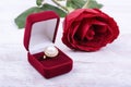 Golden pearl ring in a red gift box and rose on white wooden background