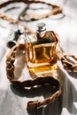 Golden perfume bottle on white fabric background with brown braided leather belt