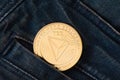 A golden physical TRON coin sticks out of the pocket of blue jeans close-up.