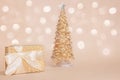 Golden present box with a silk bow against gold sparkling christmas pine tree on pastel background with beautiful Royalty Free Stock Photo