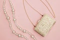 Golden purse and pearl necklace on pink background