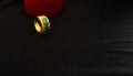 Golden ring with green stones in front of the heart-shaped box isolated on black background Royalty Free Stock Photo