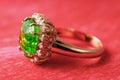 Golden ring with a large emerald and a path of small cubic zirconias on a red abstract background