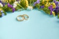 Golden rings with colored flowers on blue background composition, wedding template Royalty Free Stock Photo