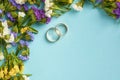 Golden rings with colored flowers on blue background composition, wedding template Royalty Free Stock Photo