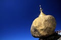 Golden Rock contrasting against blue sky. Gold painted boulder balancing on the edge of steep high