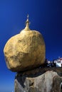 Golden Rock contrasting against blue sky. Gold painted boulder balancing on the edge of steep high mountain