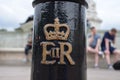 Royal symbol on a black London pole, tourists sitting in the background