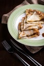 Golden Russian pancakes with cream plate close-up dark background.