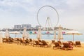 Golden sand between rows of sun chairs and beach umbrellas in the JBR district in Dubai. Ferris wheel at the background.