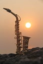 The golden saxophone alto stands on a black stone, against a background of sunset. Silhouette of saxophone against the sky. Roman