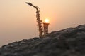 The golden saxophone alto stands on a black stone, against a background of sunset. Silhouette of saxophone against the sky. Royalty Free Stock Photo