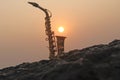 The golden saxophone alto stands on a black stone, against a background of sunset. Silhouette of saxophone against the sky.