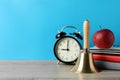 Golden school bell, apple, alarm clock and books on wooden table against turquoise background, space for text Royalty Free Stock Photo