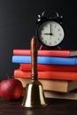 Golden school bell, apple, alarm clock and books on wooden table near blackboard Royalty Free Stock Photo