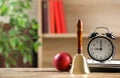 Golden school bell, apple, alarm clock and notebooks on wooden table in classroom, space for text Royalty Free Stock Photo