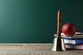 Golden school bell, apple and books on wooden table near green chalkboard. Space for text Royalty Free Stock Photo