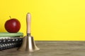 Golden school bell, apple and notebooks on wooden table against yellow background, space for text Royalty Free Stock Photo