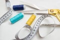 Golden scissors, blue, blue and yellow threads, measuring tape lying on a white background, a set for cutting and sewing