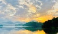 Golden Serenity: Dramatic Sunrise Over a Tranquil Lake, Embraced by Hills and Trees Royalty Free Stock Photo