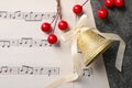 Golden shiny bell with white bow, decorative berries and music sheets on grey textured table, flat lay and space for text. Royalty Free Stock Photo