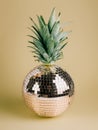 Golden shiny disco ball with pineapple leaves on the top isolated on beige background. Christmas tree ornament as tropical fruit