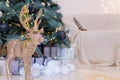 Golden shiny reindeer toy with white baubles, wrapped presents and decorated fir-tree, sofa on blurry background. Winter Royalty Free Stock Photo