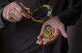 Golden and silver coins of crypto currency in male hand palm with magnifying glass, close up. Pile of bitcoin and other