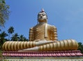 A golden sitting Buddha opposite a blue sky