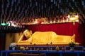 Golden statue of a reclining Buddha. Closed eyes. Ceiling decorated with paper lanterns, colorful lanterns hanging. Offerings to Royalty Free Stock Photo