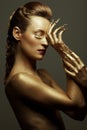 Golden statue of Valkyrie concept. Arty portrait of model with golden healthy skin and shiny lashes. Perfect sporty body. Golden