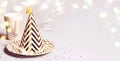 Golden striped cone hat and other party accessories. Bokeh lights and confetti. Banner format