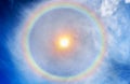 Golden sun on blue sky background with many flames and huge rainbow halo at noon