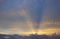 Golden sun rays from behind clouds stretch across the sky above Royalty Free Stock Photo