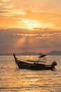 Golden sun rays and local empty thai longtail boat under them in sea water at beautiful orange sunset