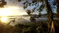 Golden sun setting over aqua fish farming bamboo structures on mountain lake.