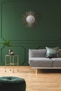 Golden sun shape like mirror on green wall of living room interior with scandinavian sofa with pillows