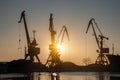 Golden sunrise illuminates industrial harbor cranes at port. Cargo for unloading, trade logistics. Heavy machinery Royalty Free Stock Photo