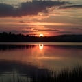 Golden sunset reflects on tranquil lake, casting mesmerizing glow