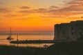 Golden sunset in the town of Dubrovnik, castle standing on the shore of a small harbour, sailboat leaving the harbour and a small Royalty Free Stock Photo