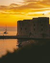 Golden sunset in the town of Dubrovnik, castle standing on the shore of a small harbour, sailboat leaving the harbour and a small Royalty Free Stock Photo