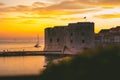 Golden sunset in the town of Dubrovnik, castle standing on the shore of a small harbour, sailboat leaving the harbour and a small Royalty Free Stock Photo