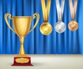 Golden trophy cup and set of medals with ribbons on blue curtain Royalty Free Stock Photo