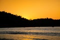 Golden tropical sunset on the beach. waves and people swimming. Mountain with palms on a background Royalty Free Stock Photo